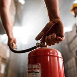 Close up of unrecognizable worker using fire extinguisher in a storage room.